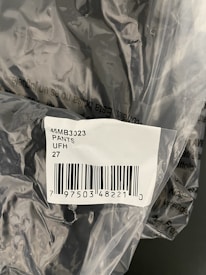 The image displays a plastic packaging containing a product labelled with a barcode sticker. The label includes text and numbers, specifically indicating '45MB3023 PANTS UFH 27' along with a barcode and a number below it.