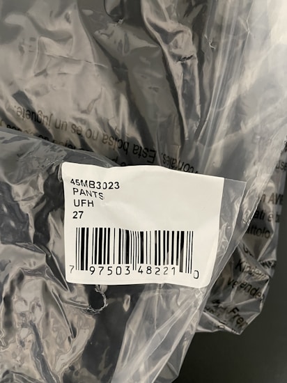 The image displays a plastic packaging containing a product labelled with a barcode sticker. The label includes text and numbers, specifically indicating '45MB3023 PANTS UFH 27' along with a barcode and a number below it.