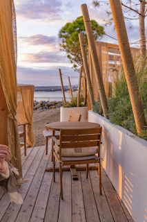 A sunlit coastal patio set with breathable mesh chairs arranged around a wooden table by the ocean.