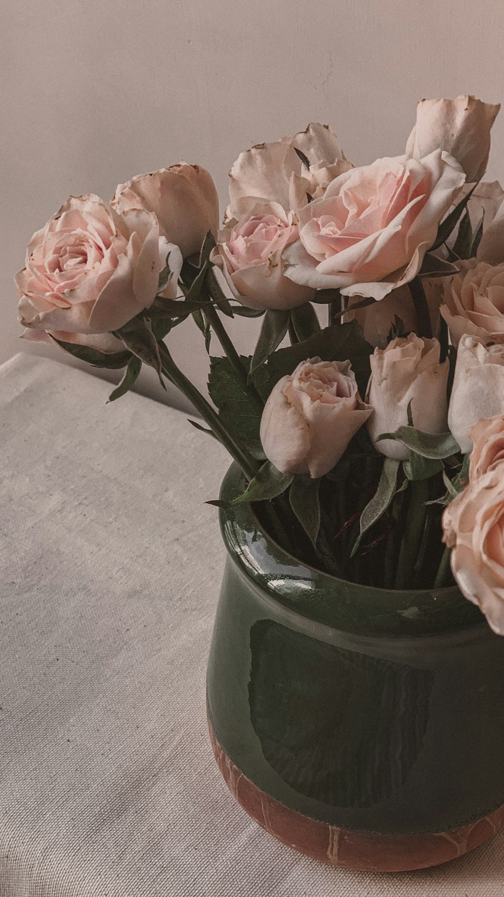 a green vase filled with lots of pink flowers