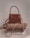 A stylish brown handbag with a structured design and looped handle, placed on top of neatly folded beige and white clothing on a neutral-colored surface.