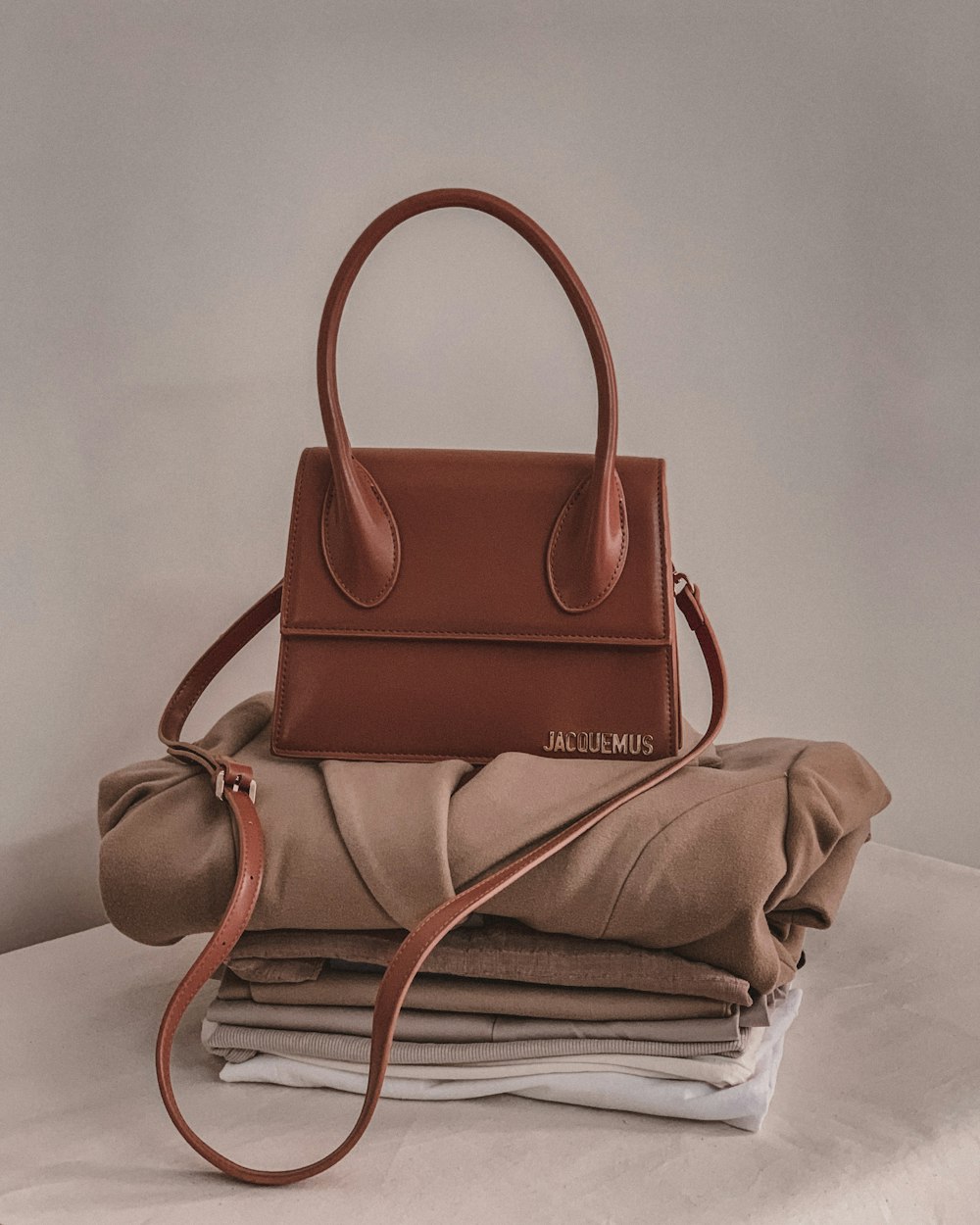 a brown purse sitting on top of a pile of folded clothes