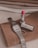 A wristwatch with a silver metal band, a ring, and a tube of red lipstick are placed on a brown piece of fabric. The fabric is layered with other textiles in the background, which are in neutral tones of beige, brown, and white.