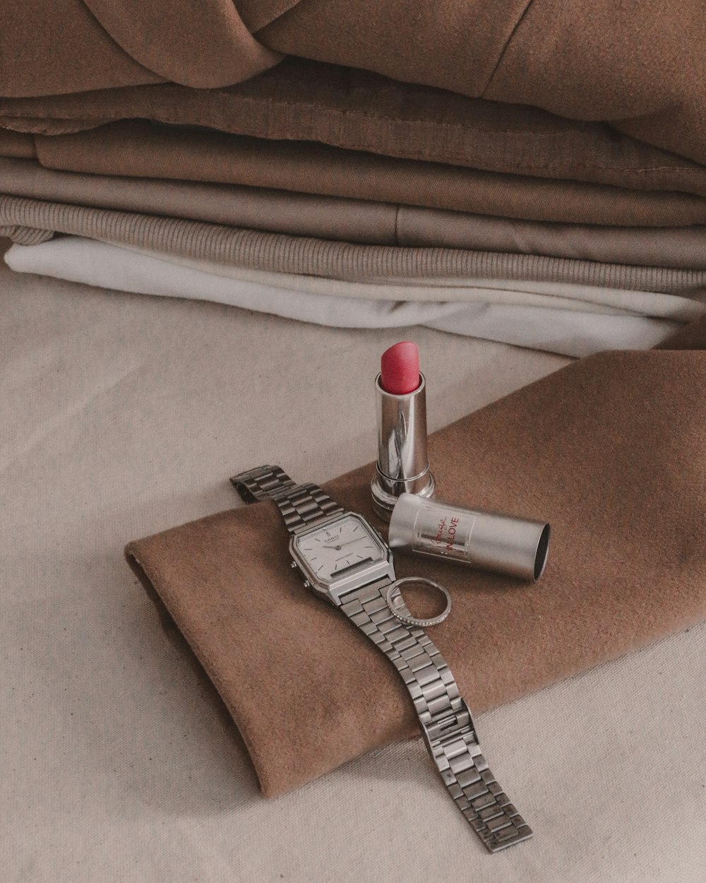 a watch, lipstick, and watch band laying on a bed