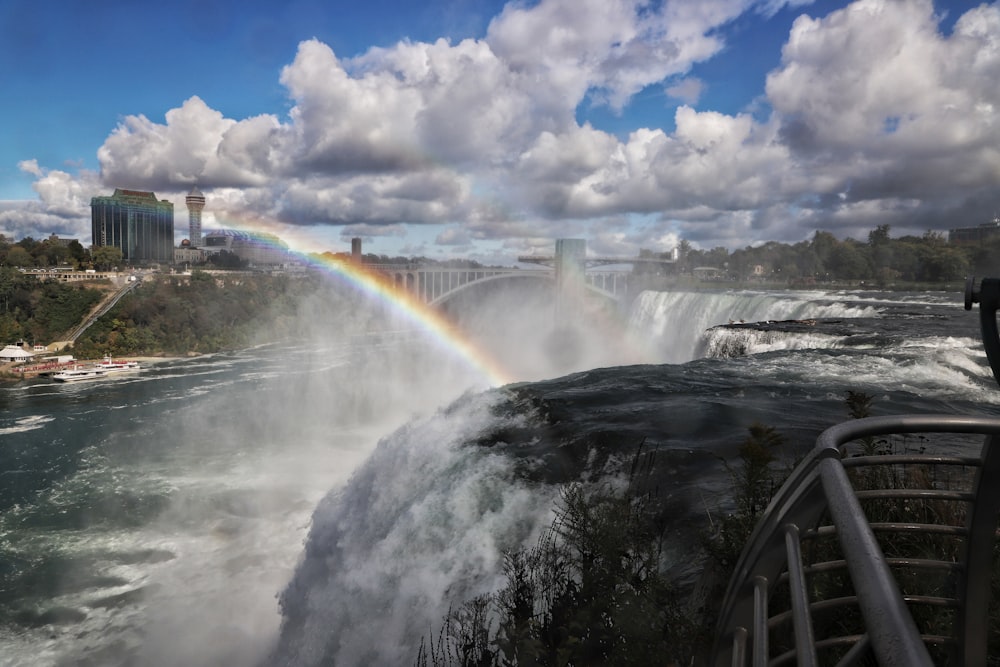 a rainbow over a waterfall with a city in the background