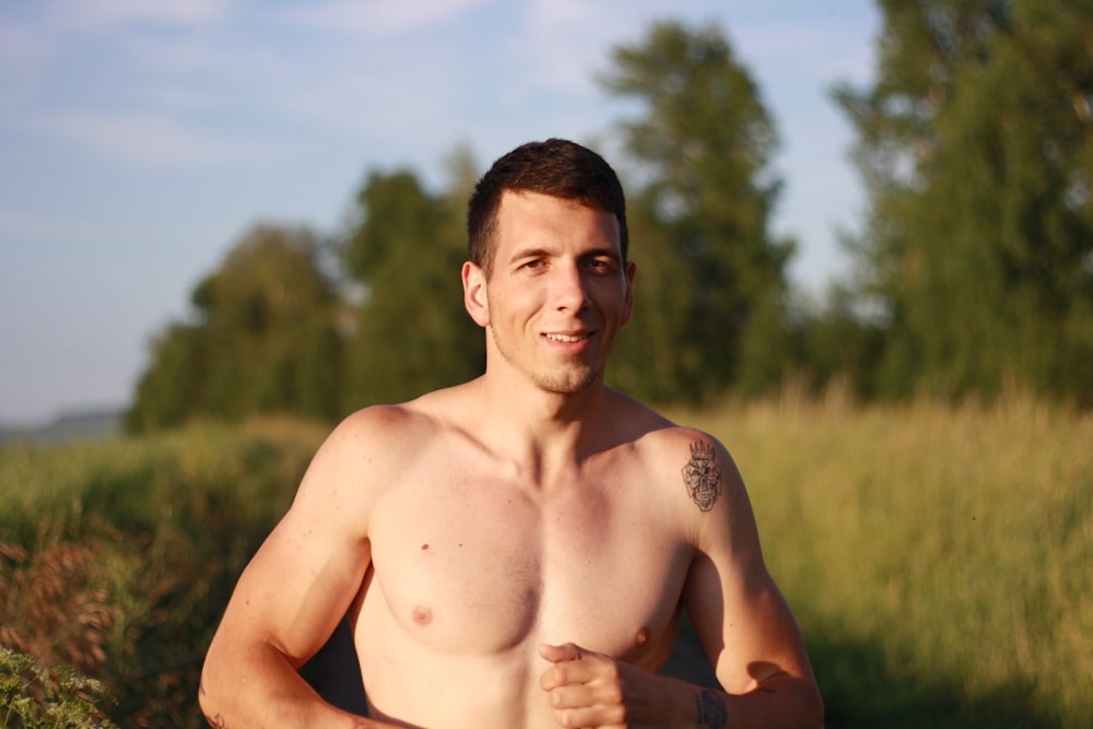 a shirtless man standing in a field with trees in the background