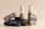 A collection of cosmetic bottles and containers are arranged artfully alongside smooth black stones. The containers are sleek, with elegant labels displaying ornate designs in golden hues against a dark background. The arrangement and lighting create a serene and luxurious aesthetic.