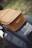 A close-up view of a vintage-style scooter seat covered in tan leather, displaying a tag labeled 'Classic'. The scooter's side panel, painted in a glossy black finish, reveals a logo reading '150 sprint v.' with a blurred green background indicating an outdoor setting.