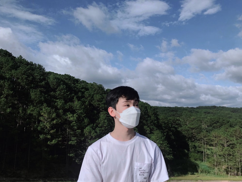 a man wearing a face mask standing in front of a forest