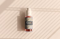 A cosmetic bottle with a pump is positioned against a background with diagonal light and shadow patterns. The bottle features a decorative label with intricate designs and the word 'Cosmetic' prominently displayed.