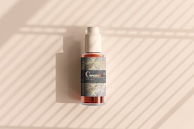 A cosmetic bottle with a pump is positioned against a background with diagonal light and shadow patterns. The bottle features a decorative label with intricate designs and the word 'Cosmetic' prominently displayed.