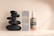 A sleek and elegant display of a cosmetic product with a pump bottle and its packaging alongside a stack of smooth black stones, set against a neutral background with soft lighting.