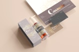 A coordinated set of cosmetic product branding materials includes a pump bottle, a rectangular box, business cards, and a leaflet. The design features elegant floral patterns in gold over grey and beige backgrounds, with the word 'Cosmetic' prominently displayed in a mix of white and copper colors.