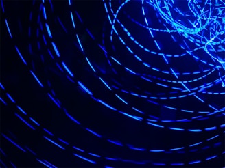 A series of bright blue light trails in circular motions against a dark background, creating a dynamic and energetic visual effect.