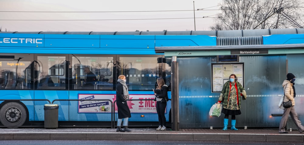 a group of people standing outside of a blue bus