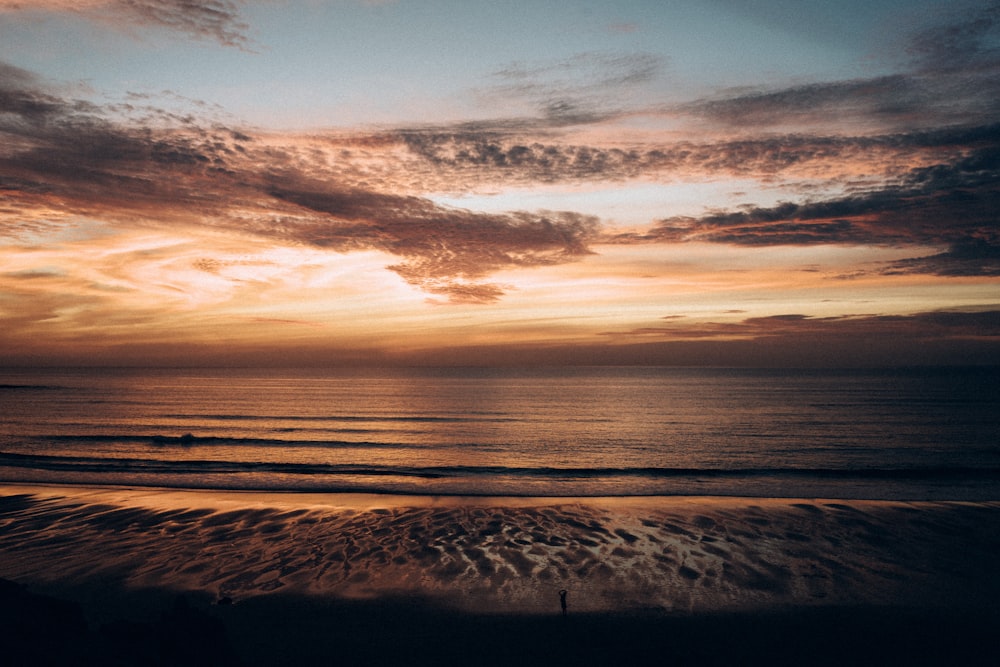 a sunset over the ocean with a person walking on the beach