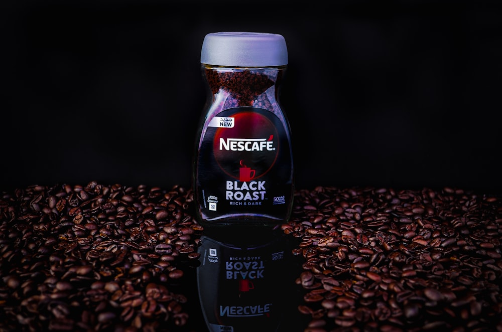 a bottle of black roast coffee sitting on top of a pile of coffee beans