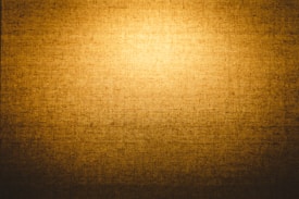 A textured golden brown surface with a woven pattern that creates a warm and rustic appearance. The lighting enhances the depth and texture of the material.