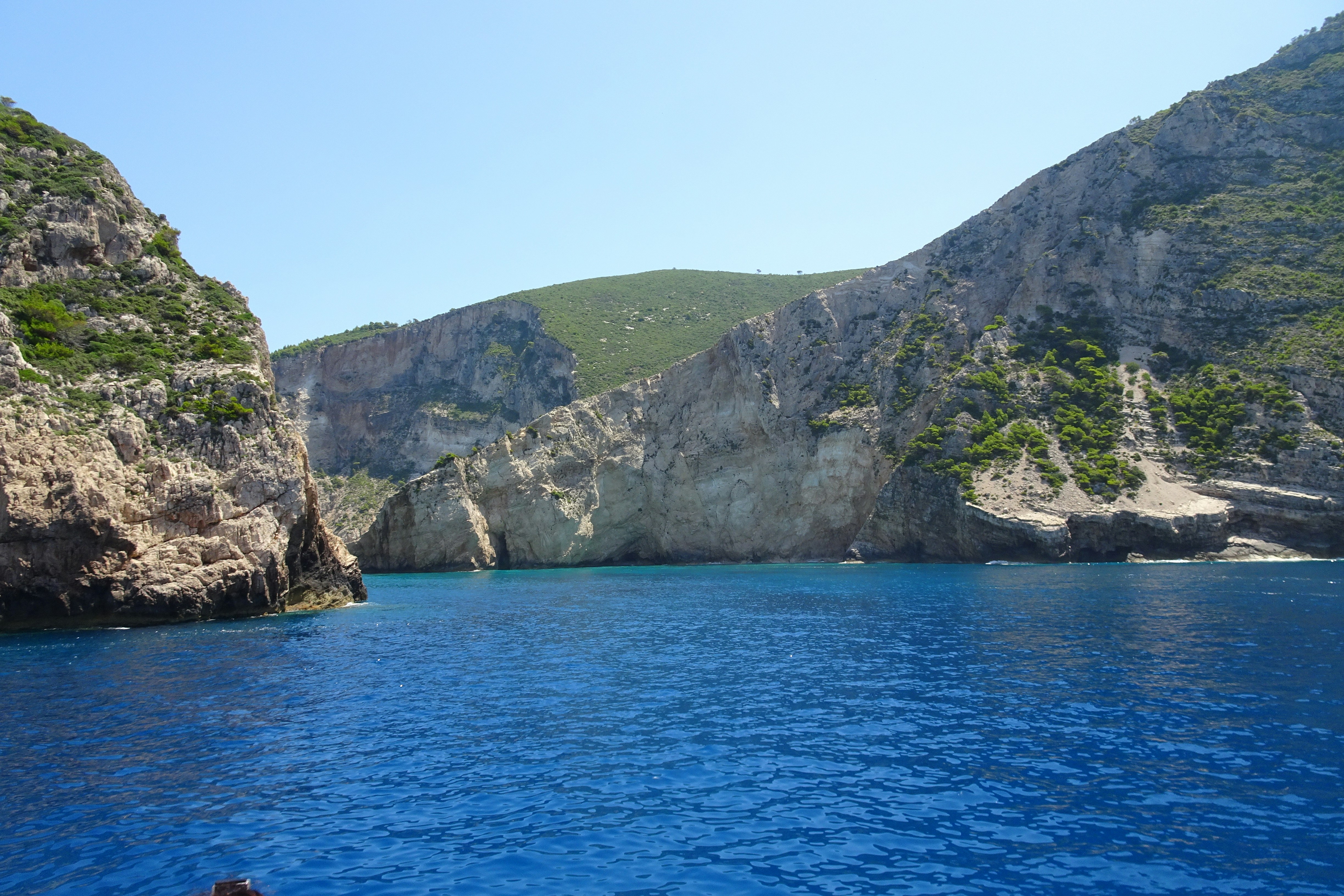 a man swimming in the ocean next to a mountain, Zakynthos Landscape Coast - Greek Island