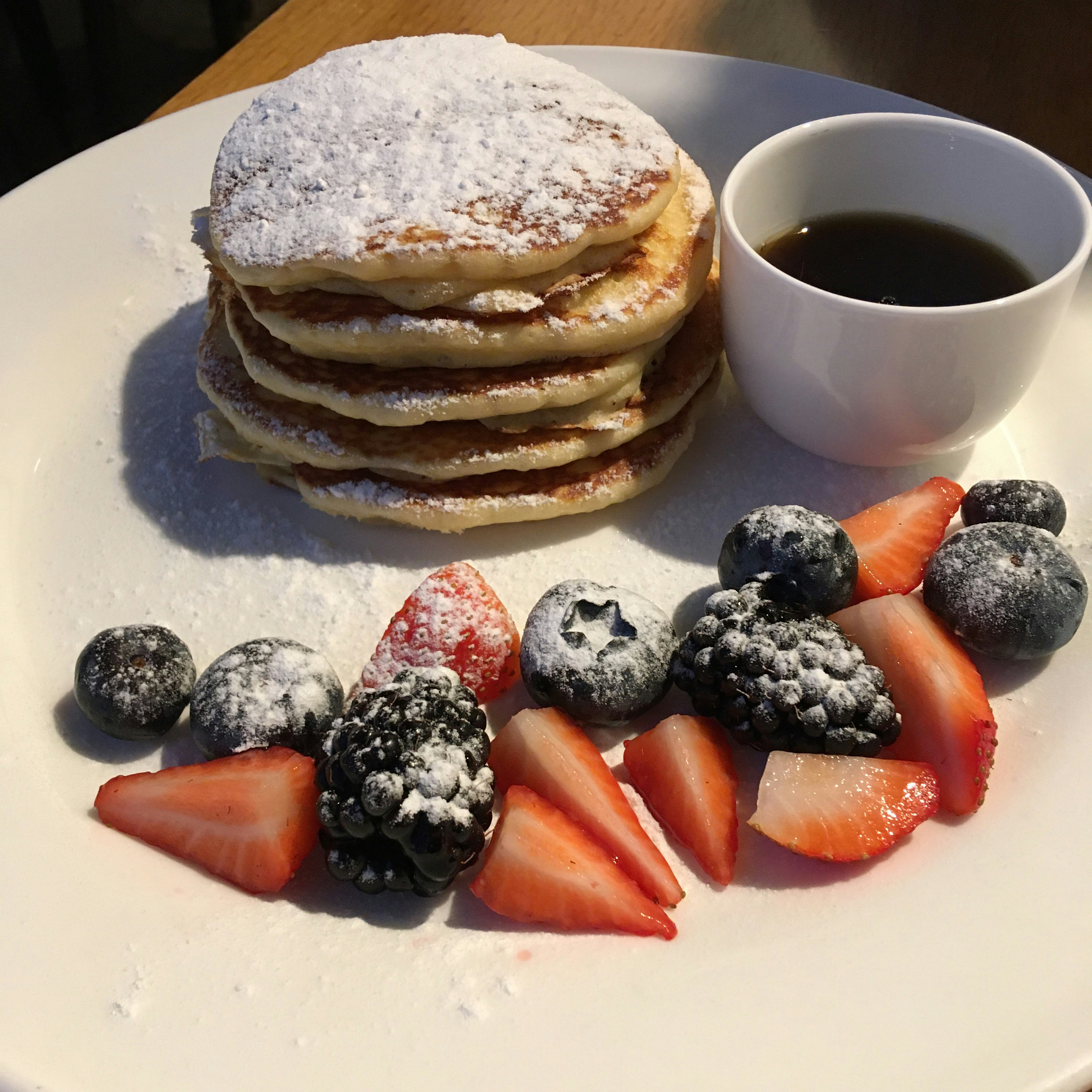 Stack of fluffy pancakes topped with melting butter and maple syrup, served on a white plate with a side of fresh berries