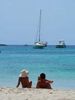 two people are sitting on the beach looking out at the water