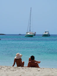 two people are sitting on the beach looking out at the water