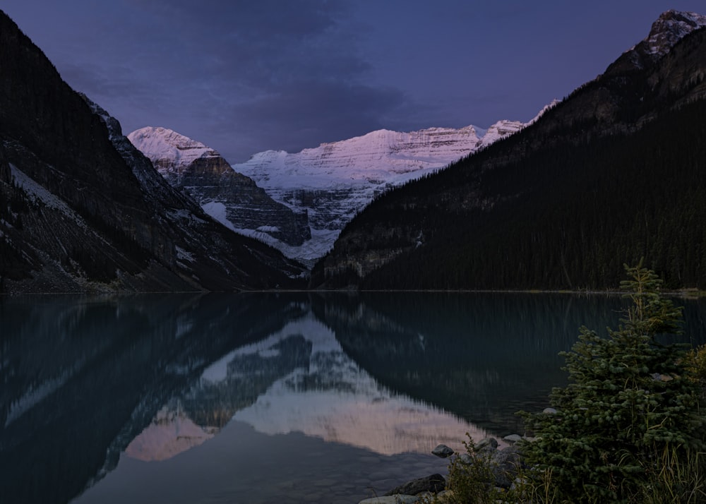 a lake surrounded by mountains under a cloudy sky