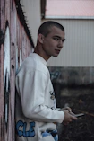 a young man leaning against a wall holding a cell phone