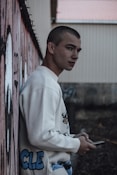 a young man leaning against a wall holding a cell phone
