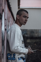 a young man leaning against a wall holding a cell phone