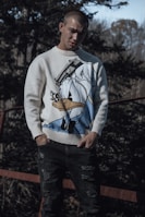 a man standing in front of a fence wearing a sweater with an image of a