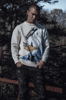 a man standing in front of a fence wearing a sweater with an image of a