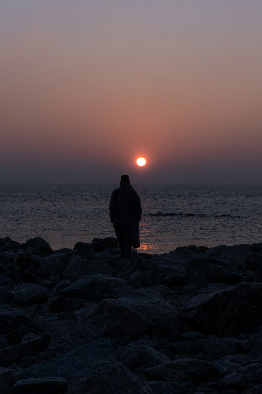 a man standing on a rocky beach watching the sun set