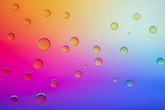 A collection of variously sized, transparent bubbles are distributed across the image. The background is composed of a vibrant gradient ranging from orange and yellow on the upper left side to blue and purple on the lower right.