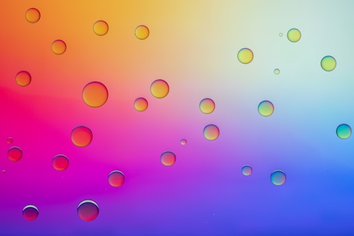 A collection of variously sized, transparent bubbles are distributed across the image. The background is composed of a vibrant gradient ranging from orange and yellow on the upper left side to blue and purple on the lower right.