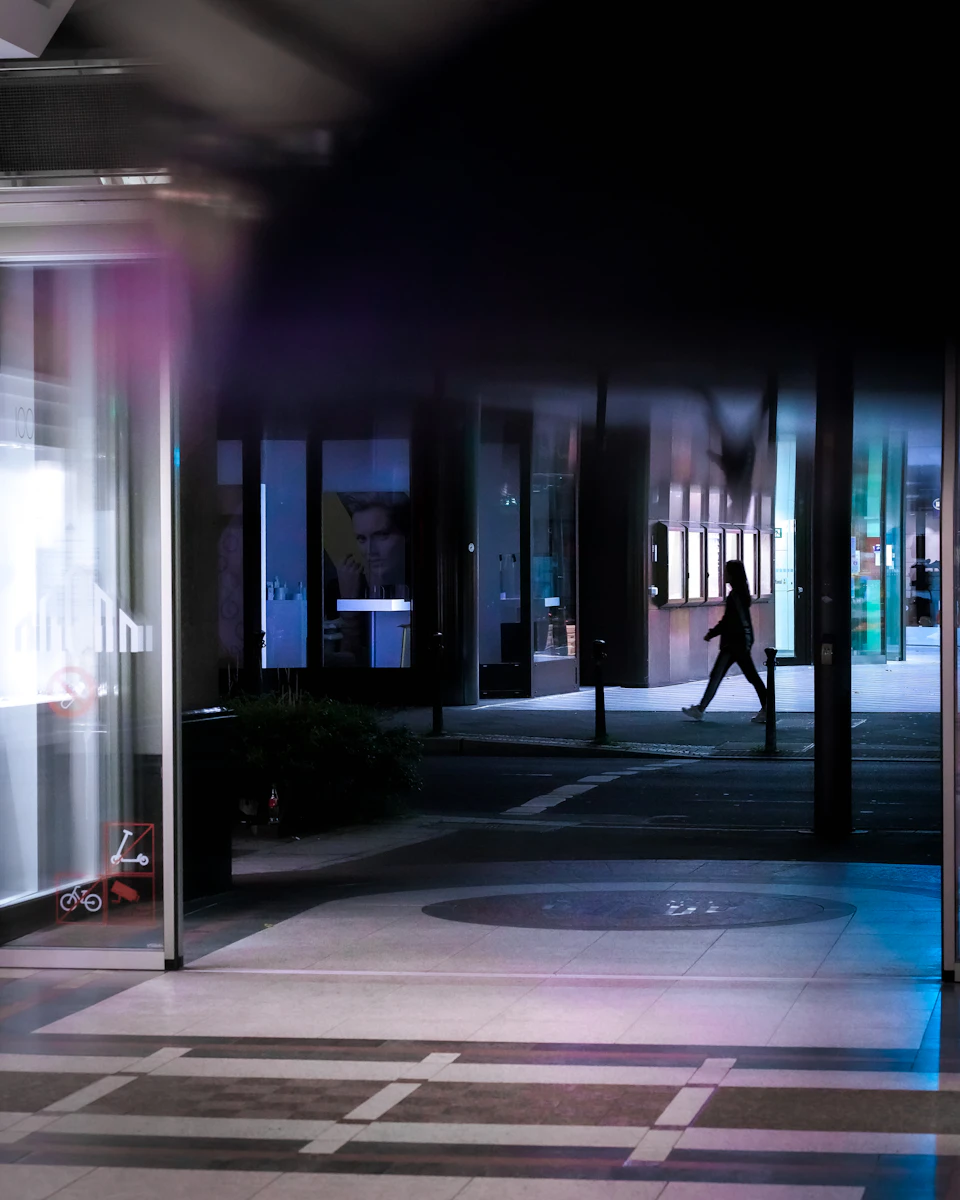 Person walking through open doorway into darkness beyond shopping mall at night