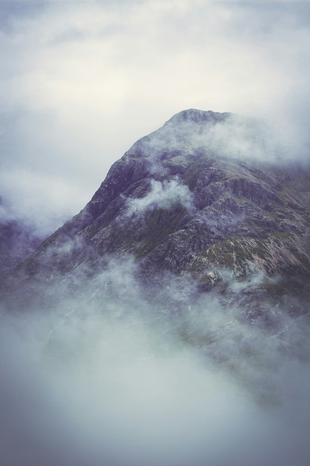 a very tall mountain surrounded by clouds in the sky