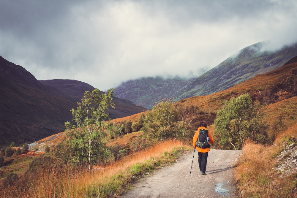 a man with a backpack and skis walking down a dirt road