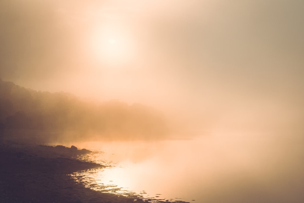 a body of water surrounded by a foggy sky