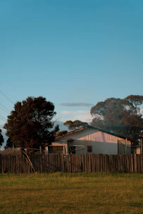 A sturdy home surrounded by a white picket fence under a clear blue sky.
