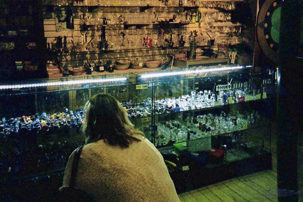 a woman sitting in front of a display case filled with bottles