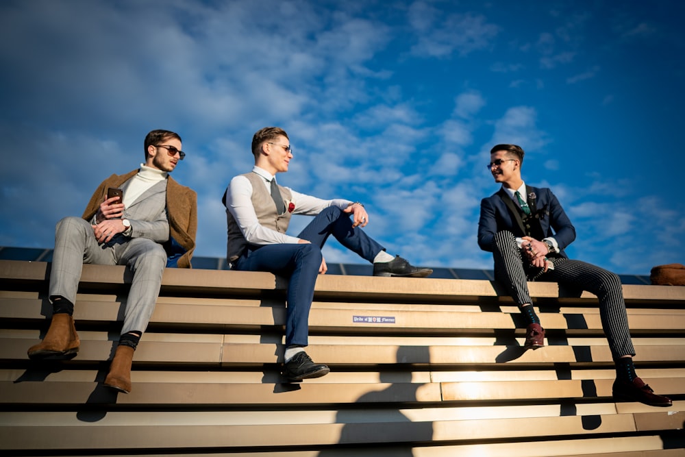 three men sitting on the bleachers of a stadium