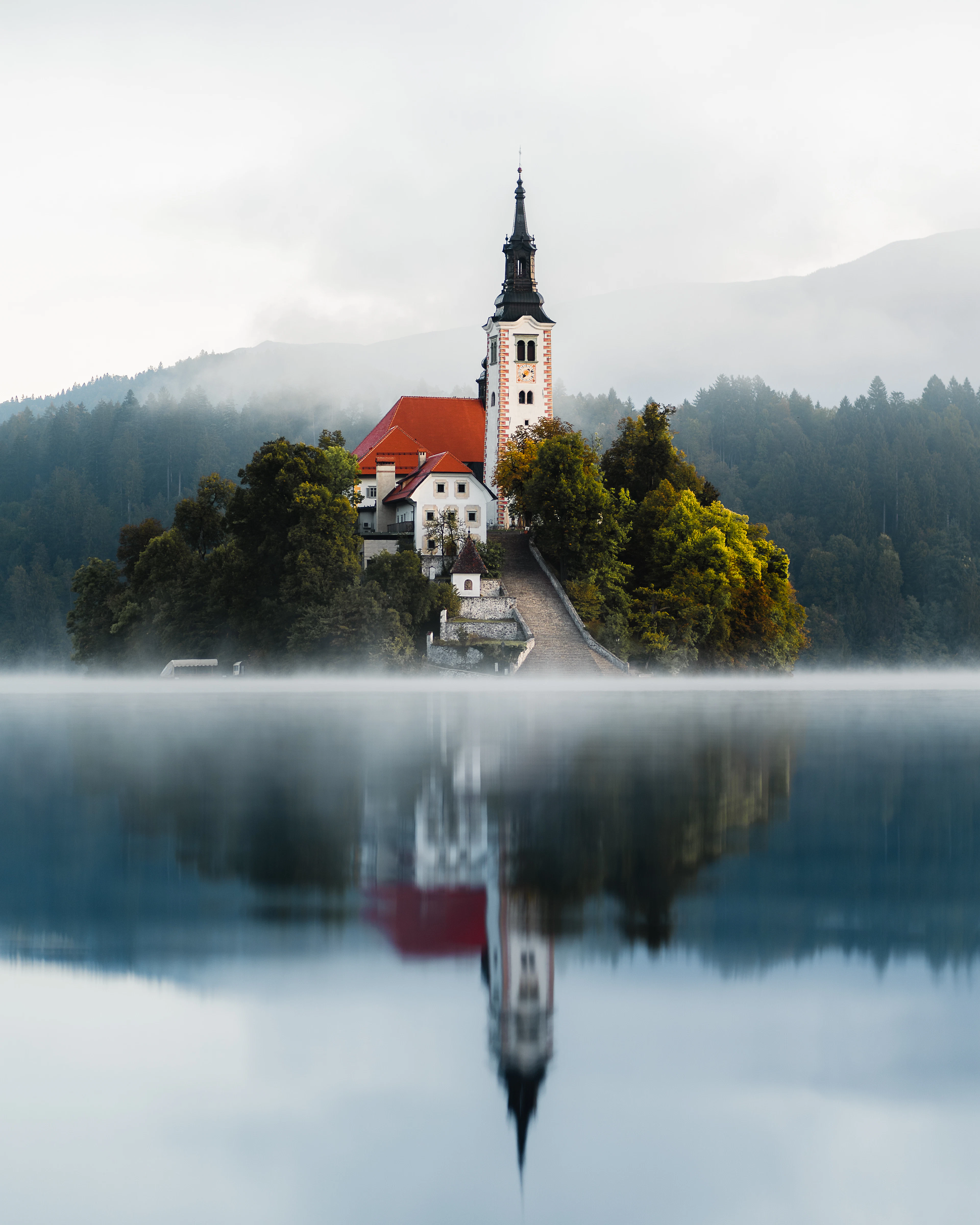 The church and bell tower on Bled Island rising out of low mist, mirrored in the still water below