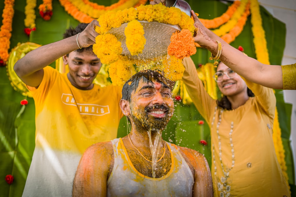 a group of people standing around a man covered in orange and yellow flowers