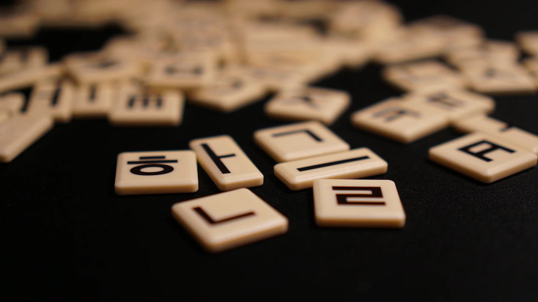 Cream letter tiles printed with single Hangul consonants and vowels, scattered across a black table