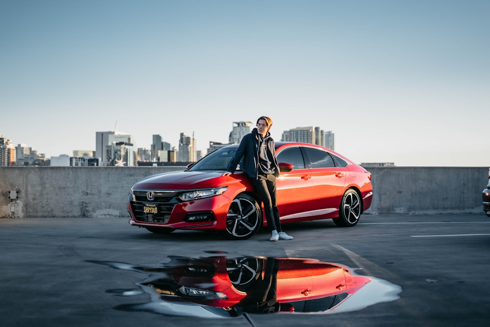 a man standing next to a red car in a parking lot