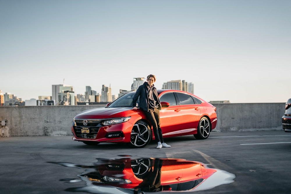 a man standing next to a red car in a parking lot