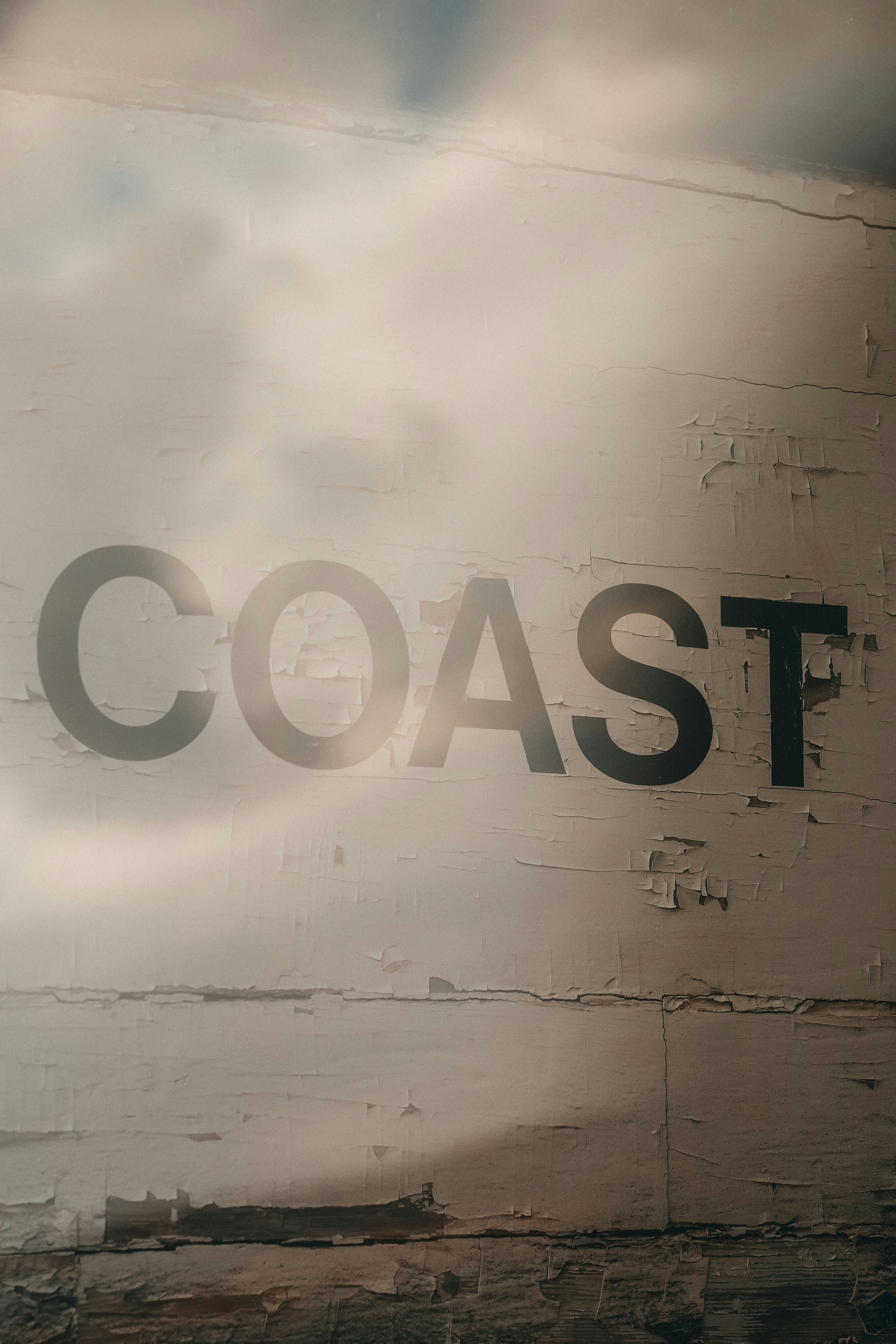 Photograph of a weathered brick wall featuring large COAST lettering with soft haze and light spill across the surface.