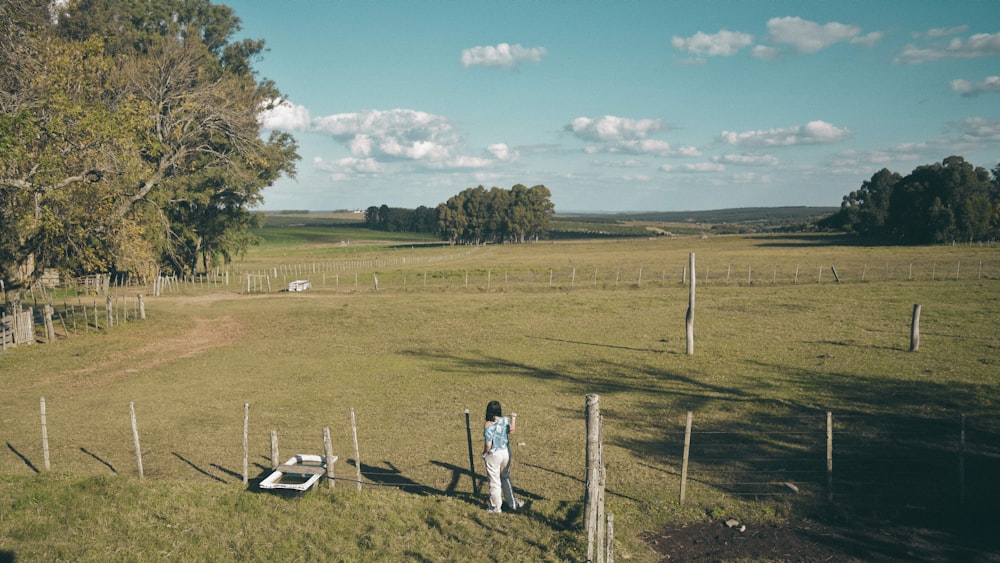 a person standing in a grassy field next to a fence