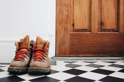 A rustic solid wood shoe rack placed beside a front door with boots and sneakers arranged.